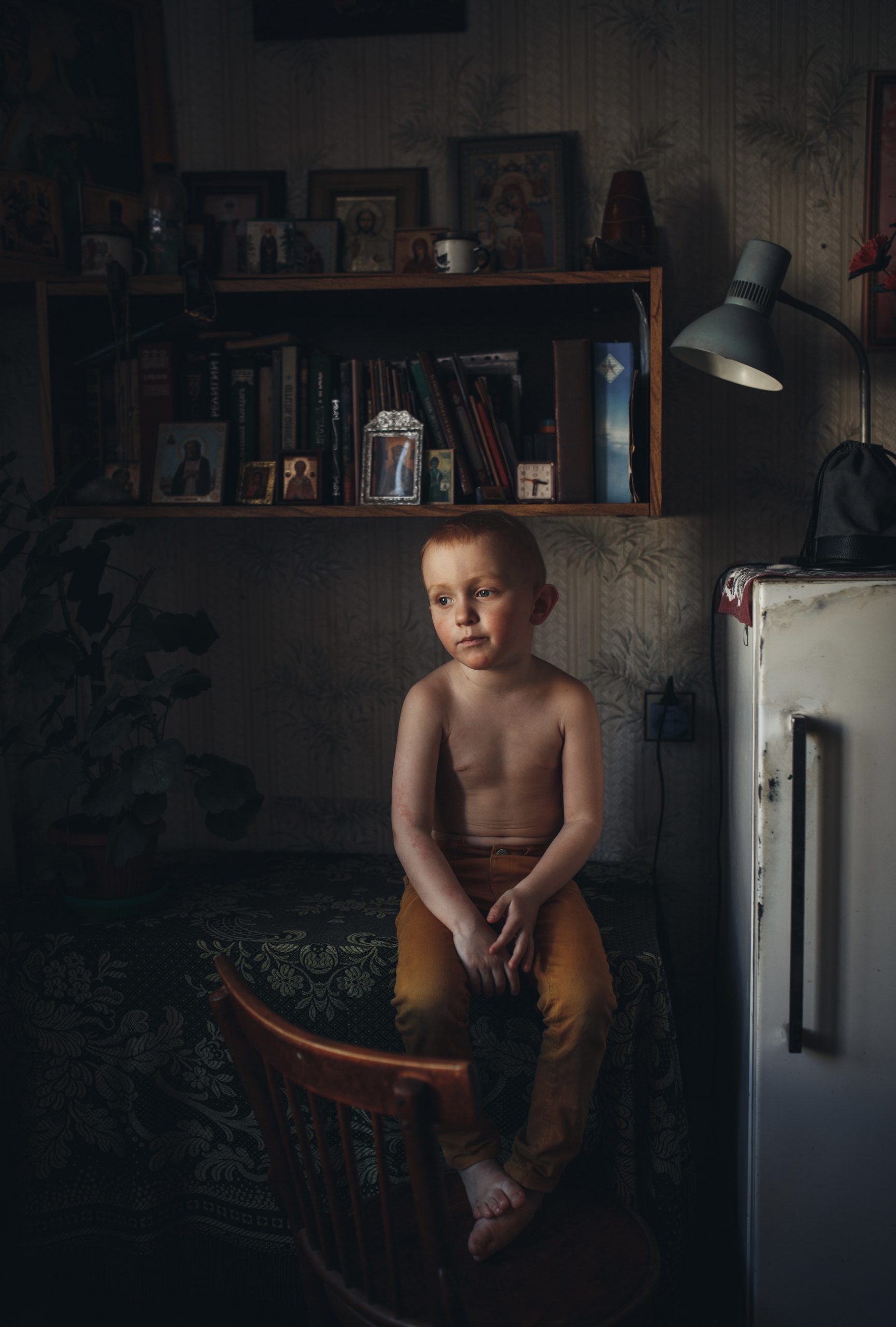 Kleiner Junge sitzt einsam auf der Küchenbank neben einem Kühlschrank