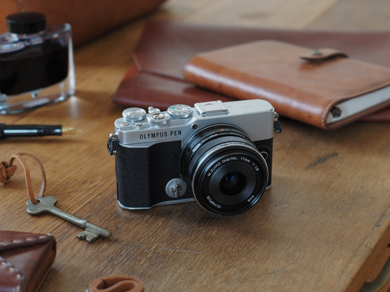 Kamera Olympus PEN E-P7 auf altem Holztisch mit Lederbuch im Hintergrund
