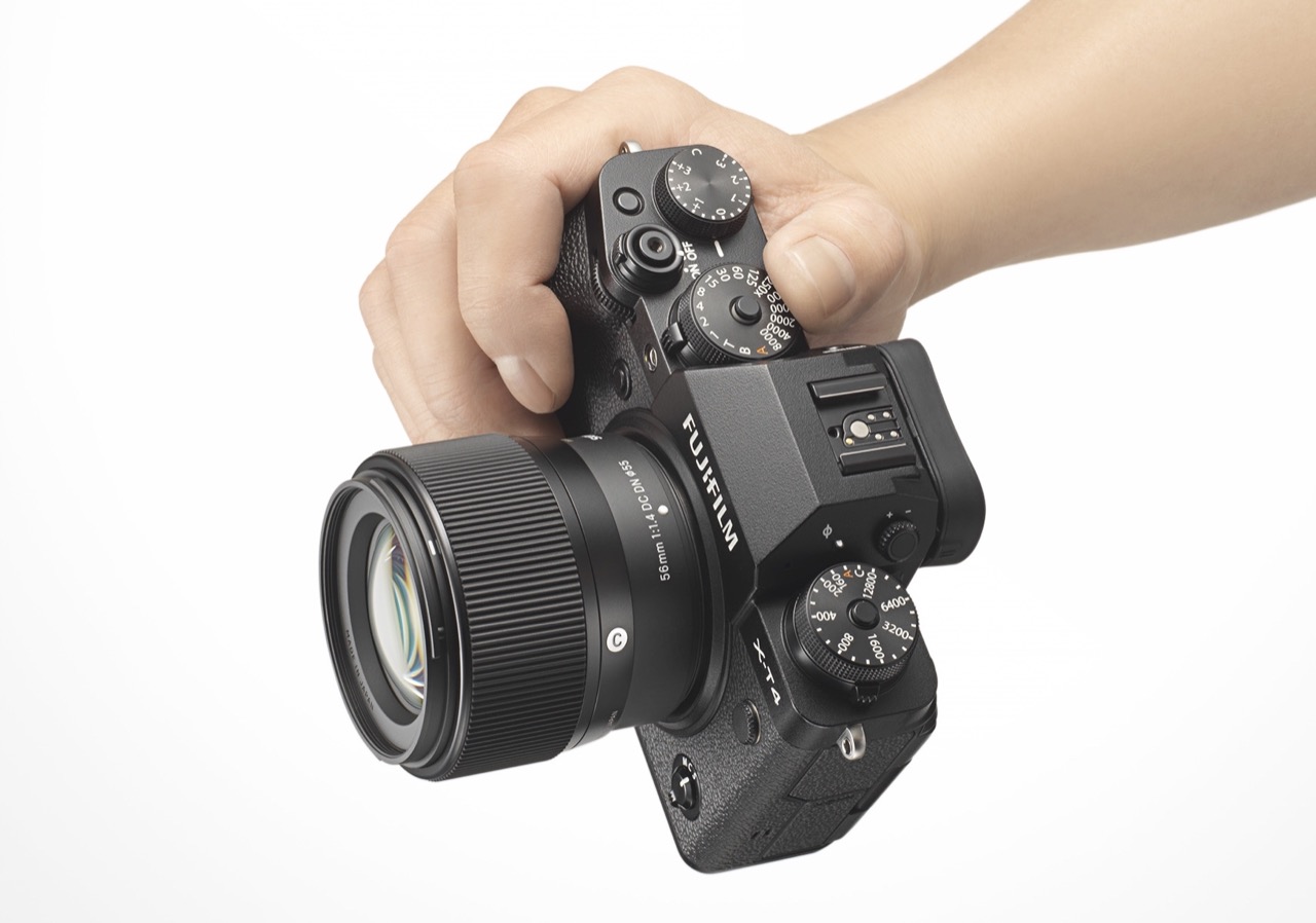 Fujifilm-Kamera mit Sigma-Objektiv wird von Hand gehalten vor weißem Hintergrund